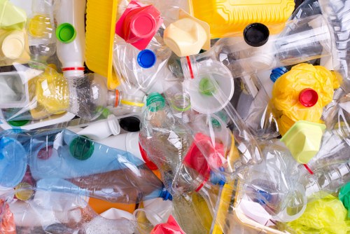 An assortment of discarded plastic bottles, caps, and containers of various sizes and colors, including clear, yellow, red, green, blue, and black, scattered across a flat surface, likely an outdoor driveway or pavement area. The plastics include PET bottles with some still partially crumpled, and a few with residual liquid or labels visible. The background shows a slightly blurred view of the surrounding environment, suggesting a domestic or commercial waste collection setting. The image emphasizes the accumulation of lightweight plastic waste commonly handled by rubbish removal services like those provided by Commercial Waste Removal Norwood, situated in the postcode area around Norwood. The overall scene reflects a typical instance of waste disposal requiring professional rubbish removal, with the plastics arranged in a somewhat layered and overlapping manner, emphasizing the need for effective waste management solutions.